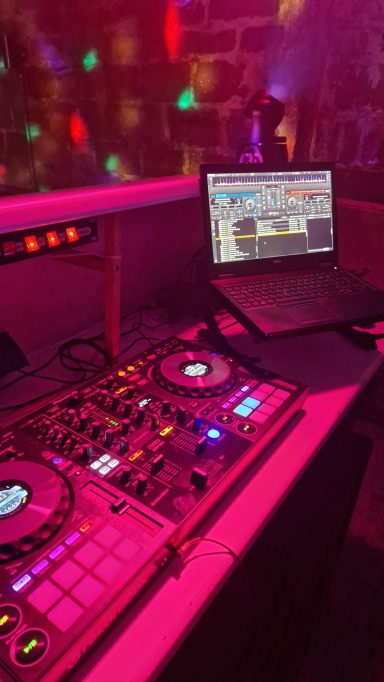 DJ-Setup mit Mischpult und Laptop in einer farbenfrohen Clubumgebung.