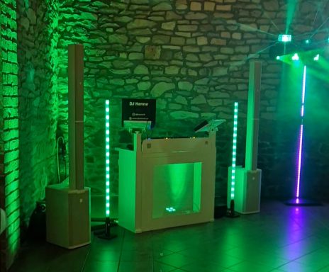 DJ-Pult mit grüner Beleuchtung und Lautsprechern in einem festlichen Raum.