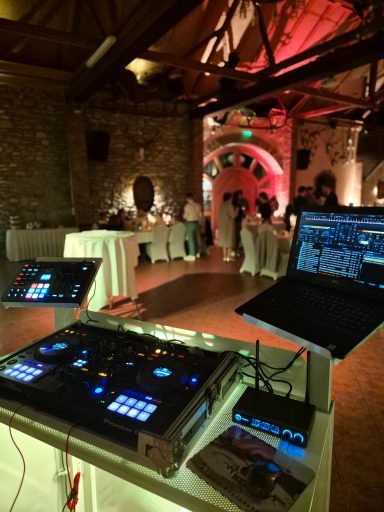 DJ-Setup mit Mischpult und Laptop in einem festlich dekorierten Veranstaltungsraum.